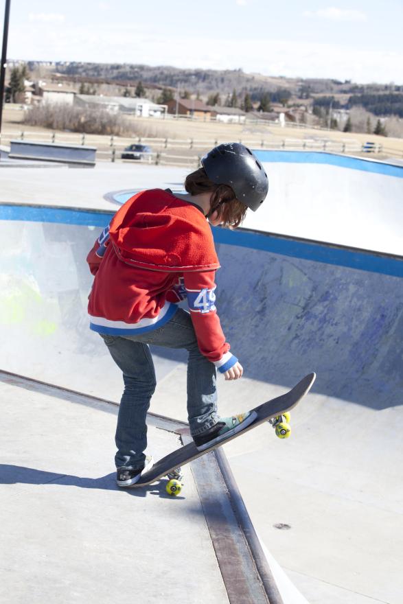 kid in orange sweater riding skateboard in the skatepark 