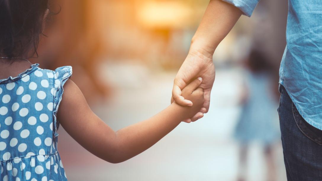 A child in a blue and white polka dot dress holding hands with an adult.