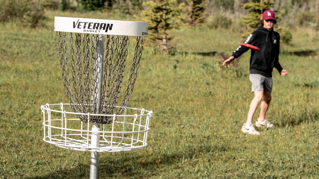 kid throwing frisbee into disc gold net 