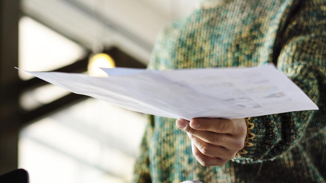 a person in a green knitted sweater hands in pieces of paper