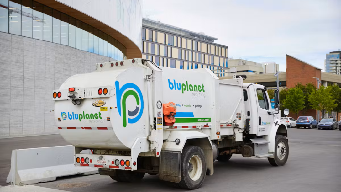 Rear of a white waste cart collection truck on street with a large BluPlanet Recycling logo. 
