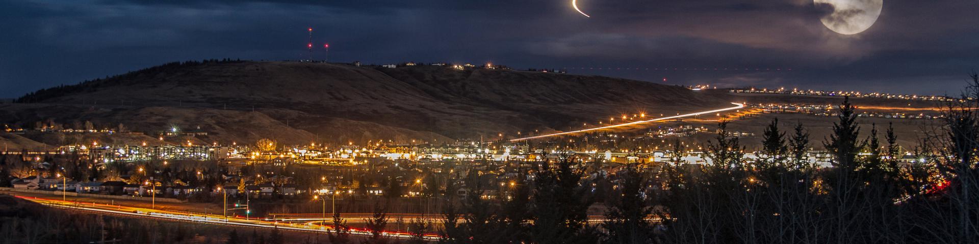 Nightscape of lit up town. There is a full moon behind a some clouds.