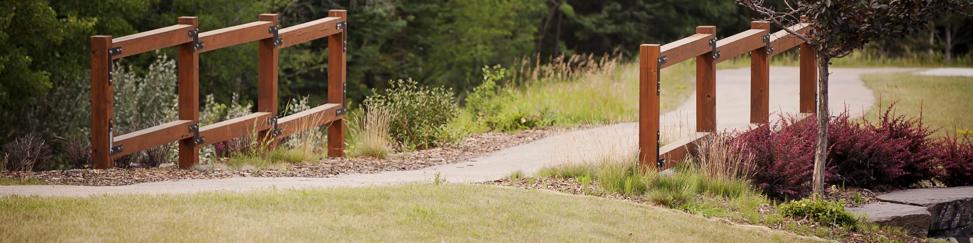 pathway with a little brown bridge and green grass surrounding 