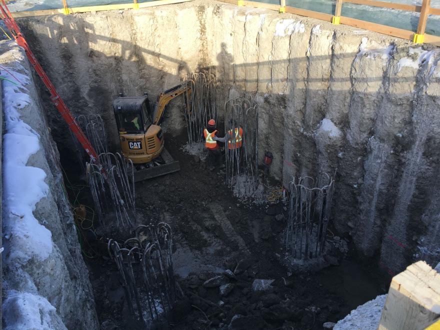 Construction workers inside bridge foundation dig site. There are rebar structure surrounding them.