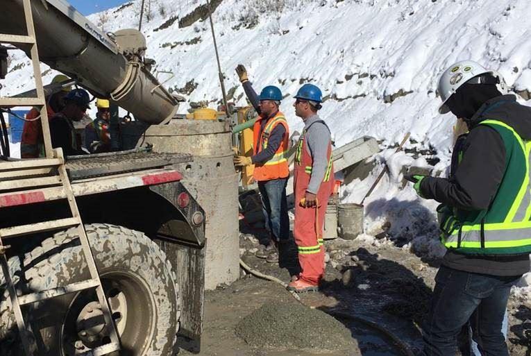 Group of construction workers standing by a cement mixing truck.