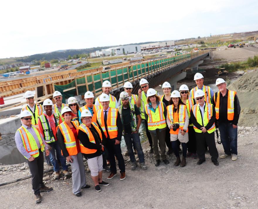Council and construction workers dressed in high-vis vests standing in front of the bridge construction site for a group photo.