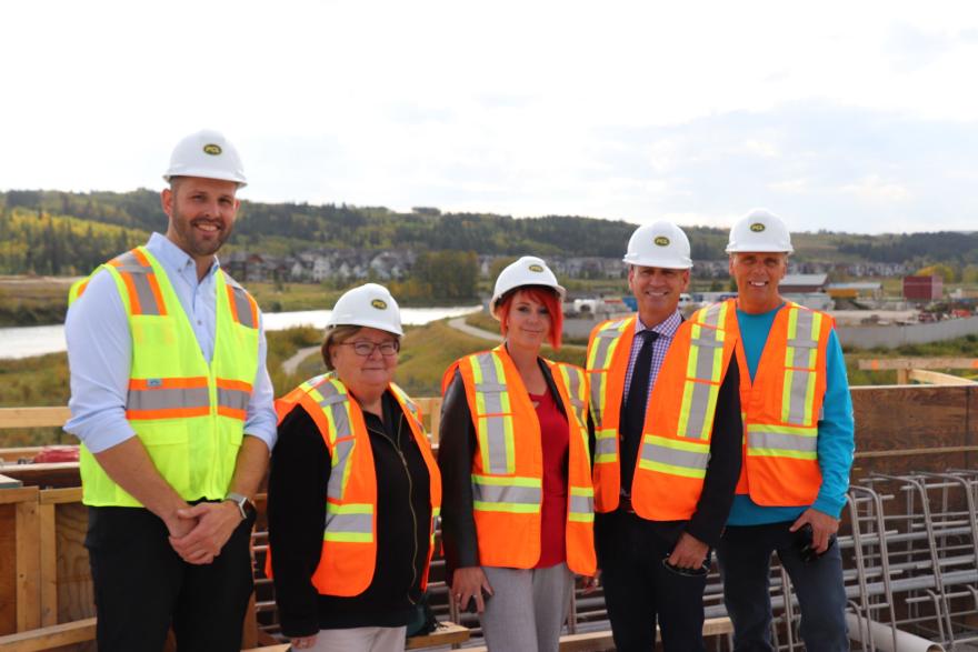 Council dressed in high-vis vests and white hardhats, standing by bridge construction.