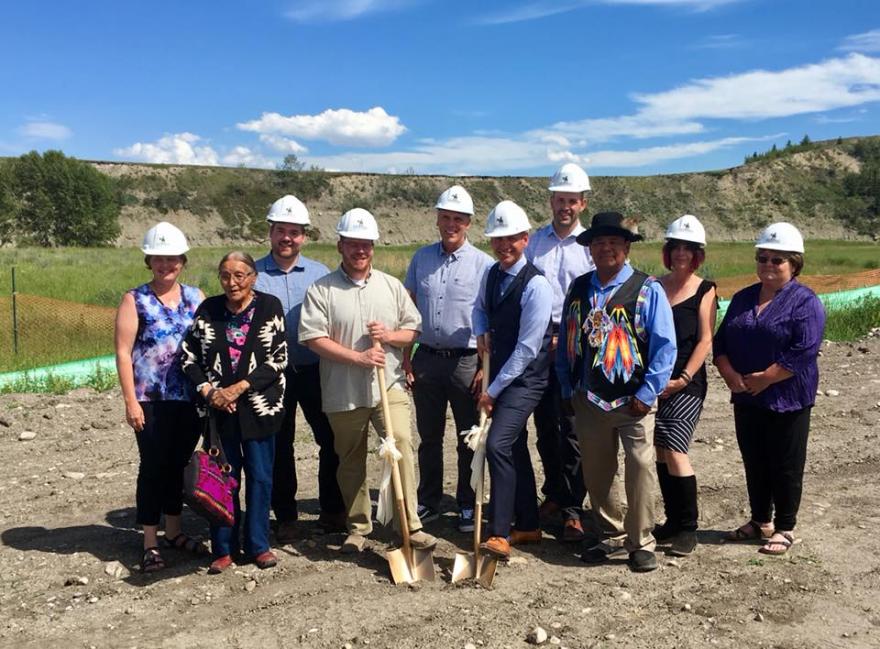 Group photo of people at a ground breaking ceremonty. There are people wearing white construction hats and holding ceremonial shovels.