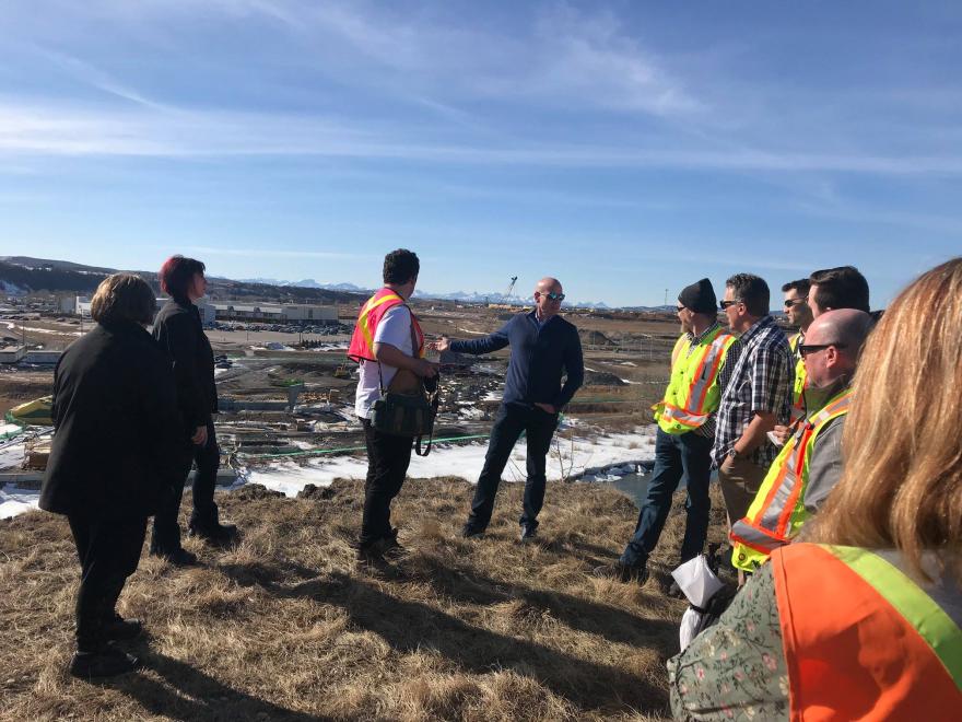 Council and construction personnel standing on the side of the bridge's construction site. The group of people are wearing high-vis vests. 