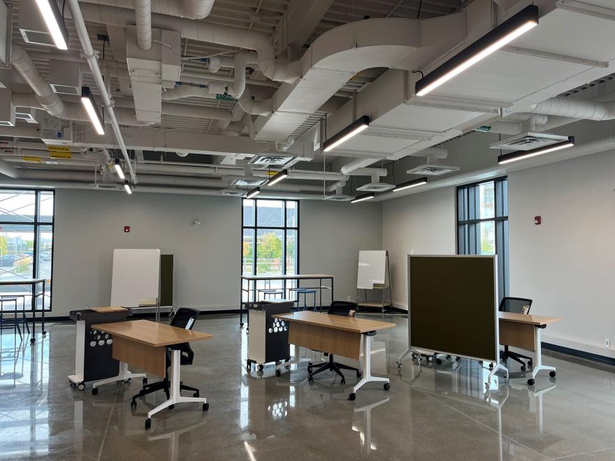 Interior of room with desks, chairs and a blackboard. The room has high ceilings and is an open space concept.