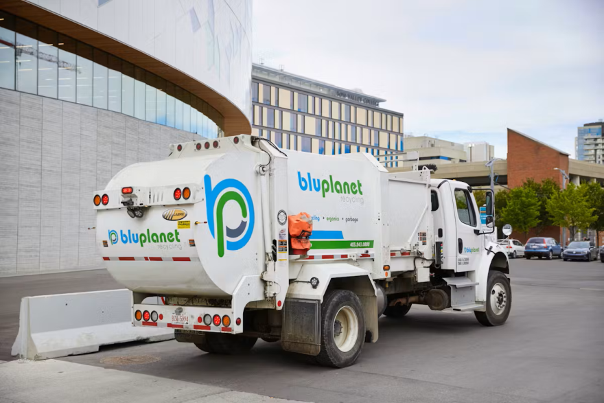 Rear of a white waste cart collection truck on street with a large BluPlanet Recycling logo. 