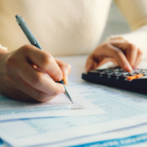 Person working on paperwork. They are using a calcuclator as they fill out the paperwork in front of them.