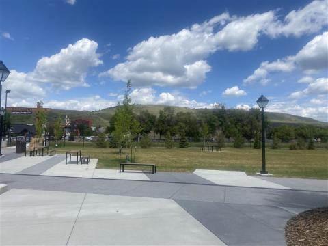 Panorama of a paved open area. There are benches and tables spread around the ares. The background has a mountain range and blue skies with white clouds.