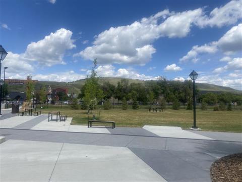 Panorama of a paved open area. There are benches and tables spread around the ares. The background has a mountain range and blue skies with white clouds.