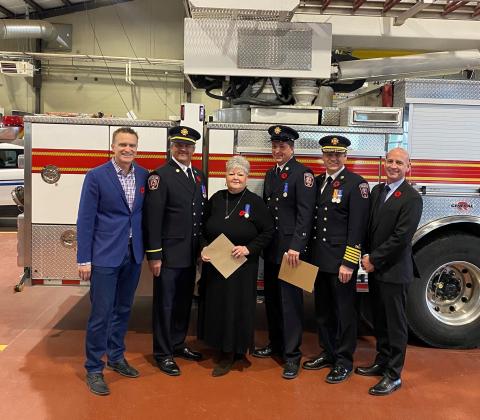 Group of Cochrane's Fire Service Members being given awards by Councillors. The group of people are standing in front of a parked fire engine.