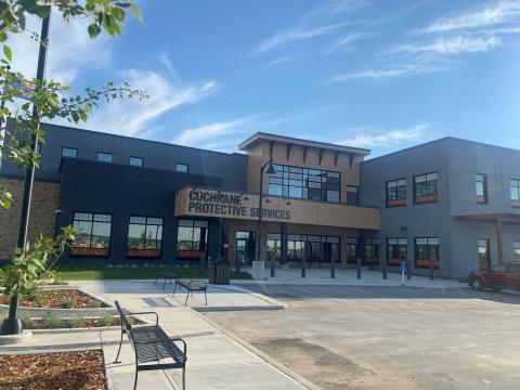 Exterior view of Cochrane's Protective Services building. In front of it there is parking lot space. There are some planters and benches near the outside of the building.