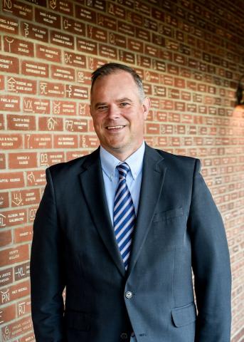 Hyndman smiling directly to camera, brick wall background