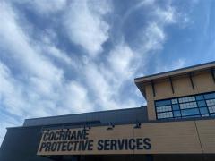 Tilted-upward view of Cochrane Protective Services building exterior. The front of the building has signage with its name on it. The building is square and and has some wooden cladding.