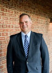 Hyndman smiling directly to camera, brick wall background