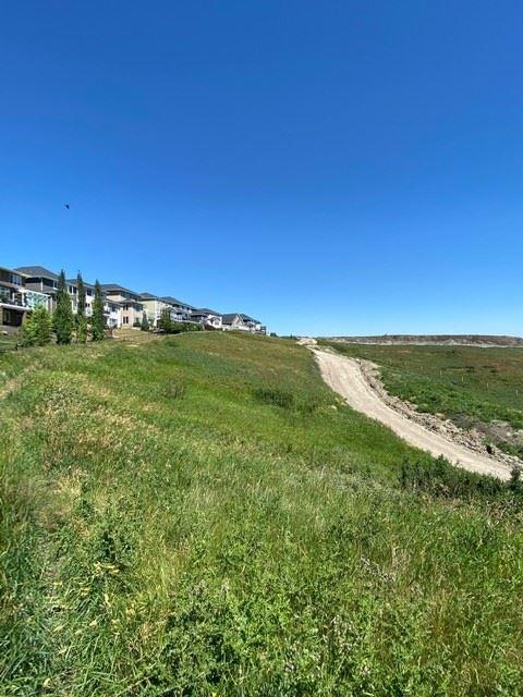 Gravel path on a hill. There are some houses to the side and over the hill. The hill is lush with green grass.