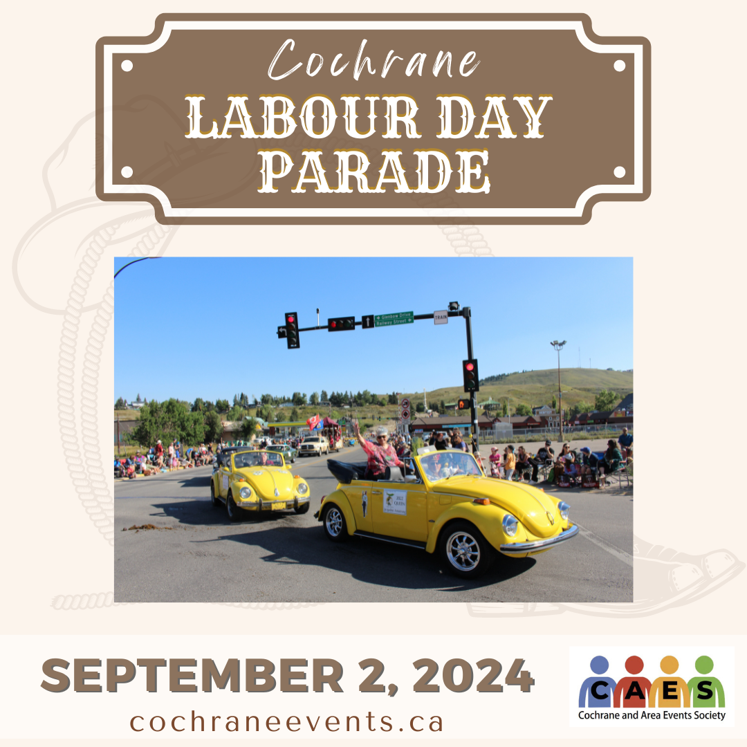 Cochrane Labour Day Parade, September 2, 2024. Picture of two yellow beetles driving through an intersection with people waving and smiling. It's a sunny day, and you can see the green hills in the background.