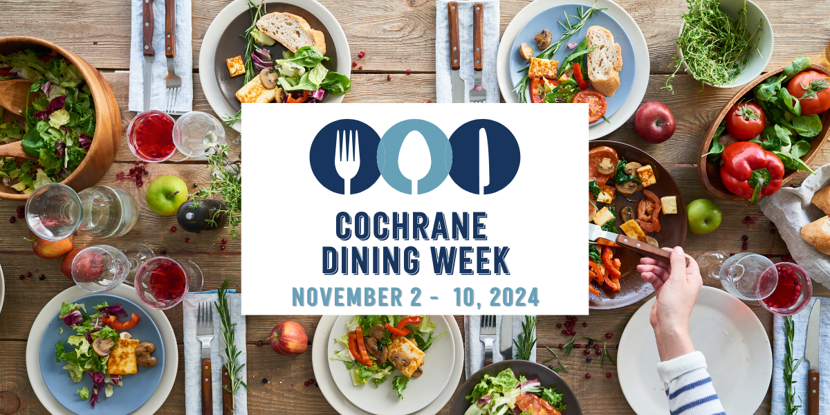 A beatiful fresh feast set on a wooden table from above. A white rectangle on top, with a blue cutlery logo, and the words Cochrane Dining Week, November 2-10